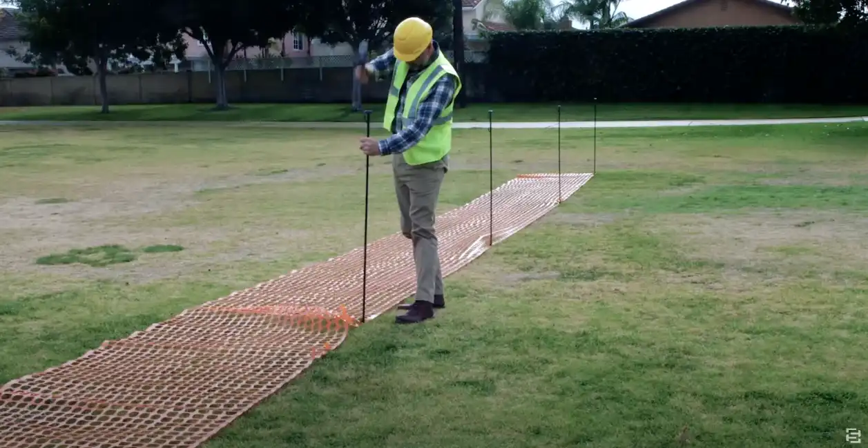 Construction worker setting up an orange safety fence in a park
