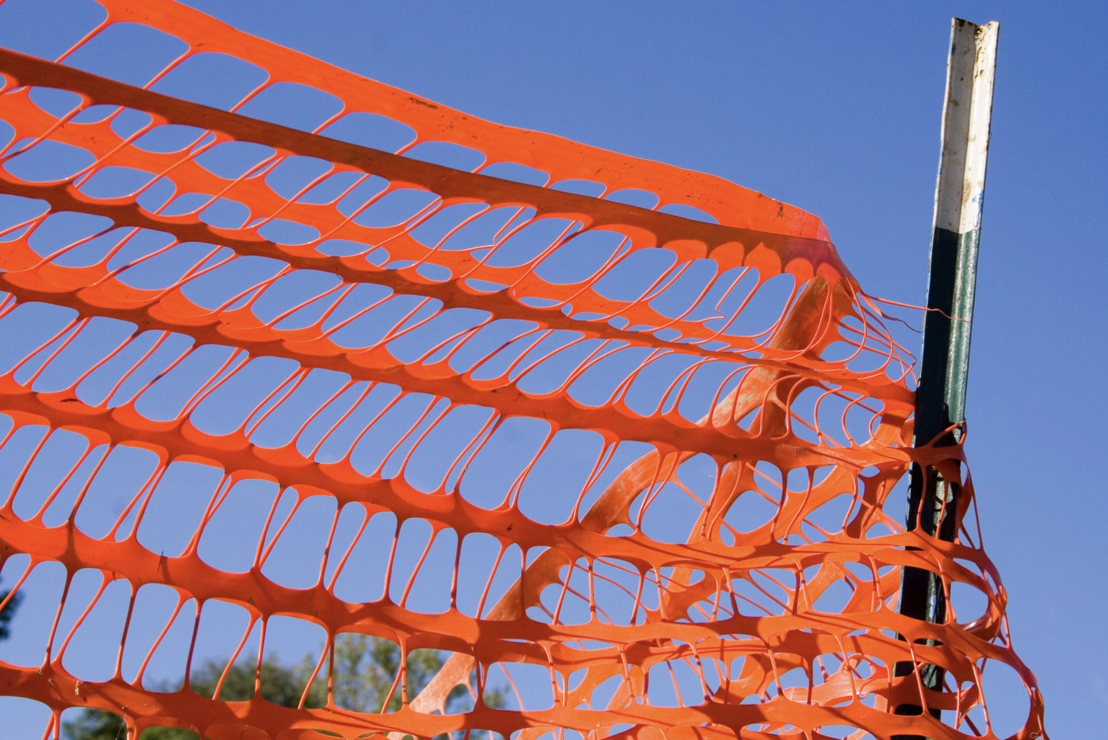 Orange plastic safety fence attached to a metal post