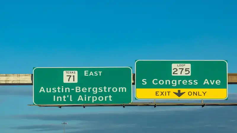 Road signs against a clear blue sky showing directions for Texas State Highway 71 East towards Austin-Bergstrom International Airport and Loop 275 for S Congress Ave with an 'EXIT ONLY' arrow.