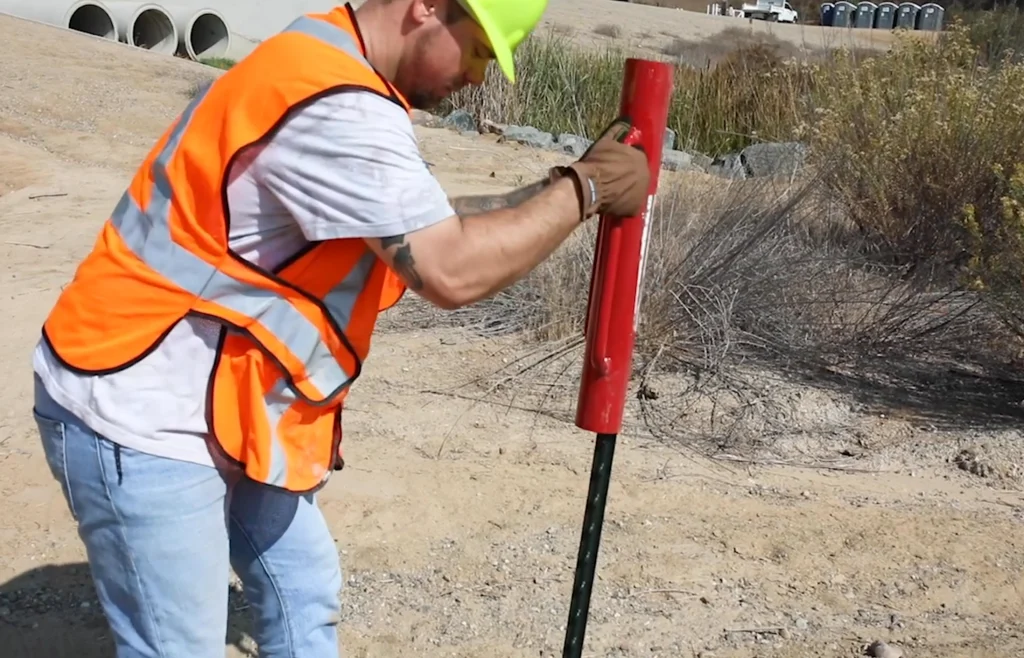 Construction worker using a post driver to install a fence post